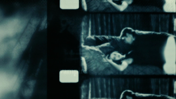 Black and white scene from Twilight with Edward lying on top of Bella on a couch with her face turned towards the viewer.