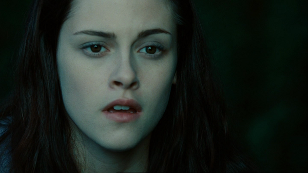 A close-up shot of Bella's open-mouthed face against a blurred green background.